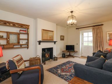 A living room with a fireplace, armchair, sofa, rug, wall shelf, small table with television, and a door with curtains at Little Lemhill Farm Cottage in Lechlade-On-Thames
