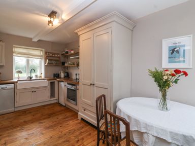 A kitchen with wooden floor white cabinets a table with flowers and two chairs at Little Lemhill Farm Cottage in Lechlade-On-Thames