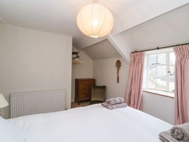 A bedroom with a bed, folded towels, a wooden dresser, a window with striped curtains, a chair, and a pendant light at Little Lemhill Farm Cottage Lechlade-On-Thames
