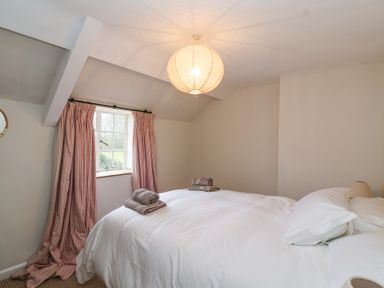 A bedroom with a double bed white bedding folded towels curtains on a window and a ceiling light at Little Lemhill Farm Cottage in Lechlade-On-Thames