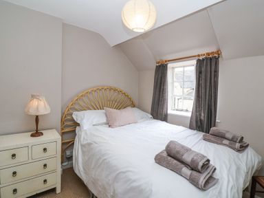 A bedroom with a bed with white linens and folded towels a nightstand with a lamp and a window with curtains at Little Lemhill Farm Cottage in Lechlade-On-Thames