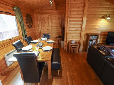 A dining area with a wooden table set with plates and glasses surrounded by black chairs and bench in a wooden cabin at Forest Lodge in Kenwick Woods