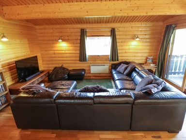 A living room with a black leather sectional sofa a television a bean bag and wooden walls at Forest Lodge in Kenwick Woods