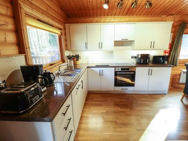 A kitchen with white cabinets dark countertops appliances and wooden walls and ceiling at Forest Lodge in Kenwick Woods