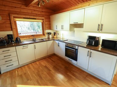 A kitchen with white cabinets and wooden walls and floor at Forest Lodge in Kenwick Woods