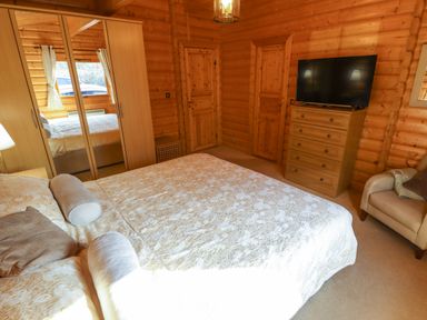 A bedroom with a bed a mirrored wardrobe a chest of drawers with a television and an armchair at Forest Lodge in Kenwick Woods