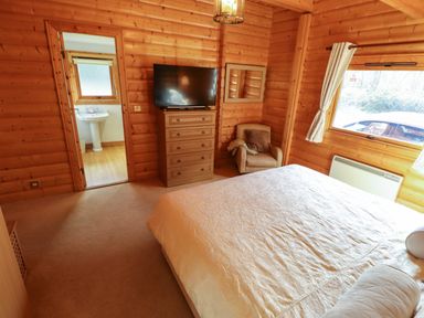 A bedroom with a bed a chair a dresser with a TV a mirror and an open door showing a bathroom at Forest Lodge in Kenwick Woods