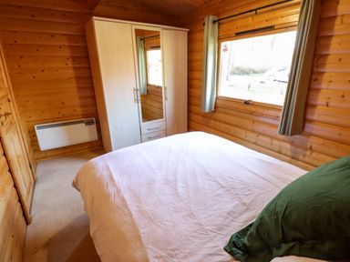 A bedroom with a bed pillow wardrobe heater and window in a wooden cabin at Forest Lodge in Kenwick Woods