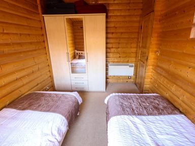 A bedroom with two single beds a wardrobe with a mirror and wooden walls at Forest Lodge in Kenwick Woods