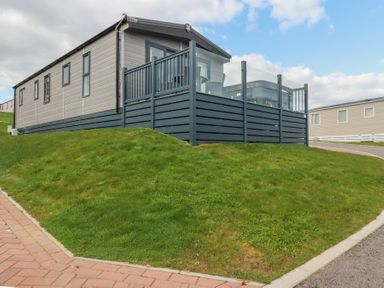 A modern mobile home with a fenced deck on a grassy slope at The Maples No 48 in Hewas Water near Sticker
