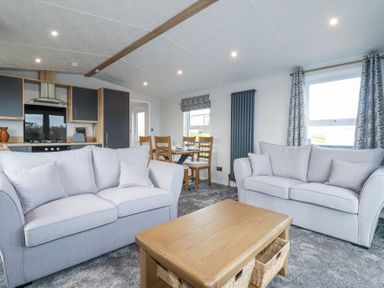 A living area with two sofas and a wooden coffee table adjacent to a dining table and kitchen at The Maples No 48 in Hewas Water near Sticker