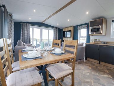 A dining area with a wooden table set for four near a living area with sofas and a wall-mounted TV at The Maples, No 48 in Hewas Water near Sticker