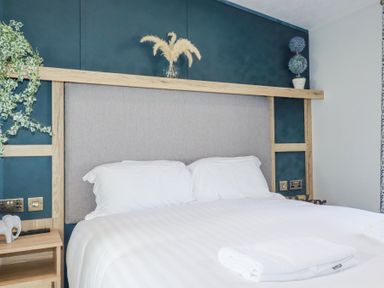 A bedroom with a white bedset and pillows a wooden headboard with plants and towels on the bed at The Maples No 48 Hewas Water near Sticker
