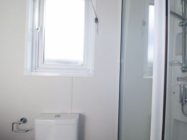 A bathroom with a toilet, toilet paper holder, window, and enclosed shower cabin at The Maples, No 48 in Hewas Water near Sticker
