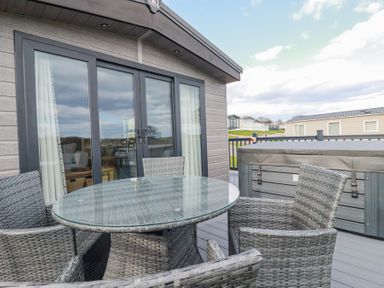 A patio with a glass table and wicker chairs next to a hot tub outside a building at The Maples No 48 in Hewas Water near Sticker