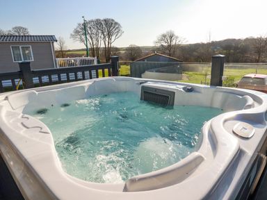 An outdoor hot tub on a deck with a railing and countryside view at The Maples No 48 Hewas Water near Sticker