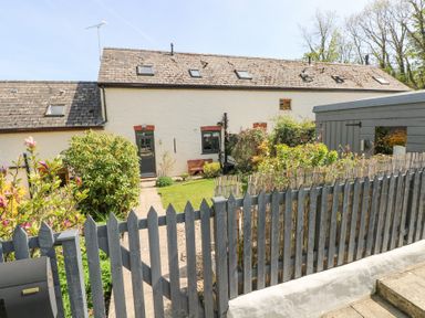 A fenced garden area with a pathway leading to a white house with multiple skylights and a gray door at 3 The Barn in Haverfordwest