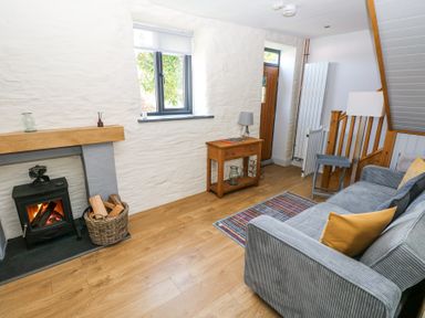 A living room with a wood burning stove basket of firewood wooden side table sofa and staircase at 3 The Barn in Haverfordwest