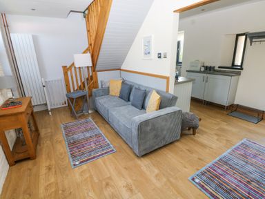 A living area with a gray sofa and colorful rugs near wooden stairs at 3 The Barn in Haverfordwest