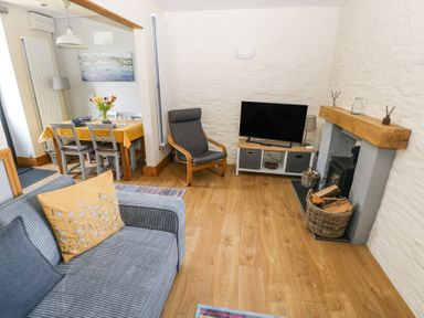 A living room with a gray sofa, armchair, television on a stand, dining table with a yellow tablecloth, and fireplace at 3 The Barn in Haverfordwest