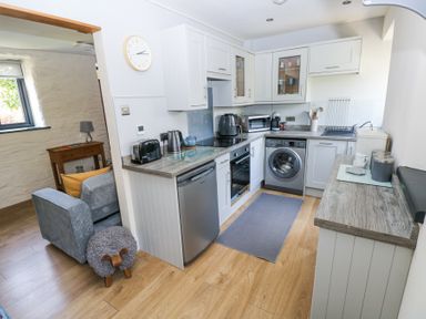 A kitchen with white cabinets, stainless steel appliances, and wooden flooring at 3 The Barn in Haverfordwest