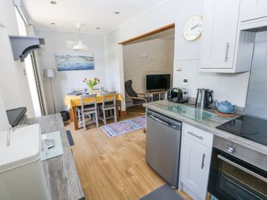 A kitchen and dining area with a yellow tablecloth on the table and a living room with a chair and television at 3 The Barn in Haverfordwest
