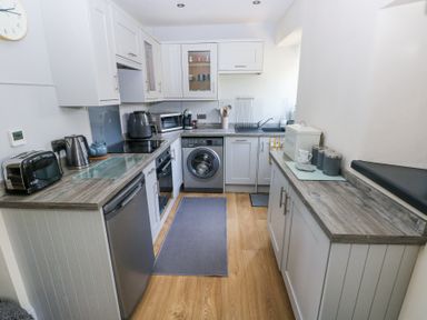 A kitchen with white cabinets, wooden countertops, a washing machine, toaster, kettle, coffee maker, and bread box at 3 The Barn in Haverfordwest