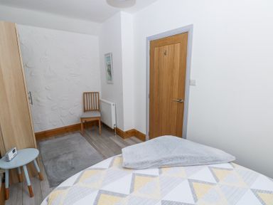 A bedroom with a wooden chair radiator wardrobe small blue table and wooden door at 3 The Barn in Haverfordwest