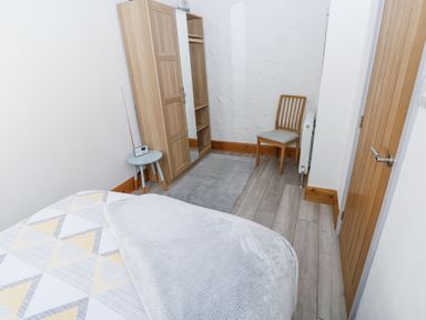 A bedroom with a bed a wooden wardrobe a small round table with a radio a chair and a door at 3 The Barn in Haverfordwest