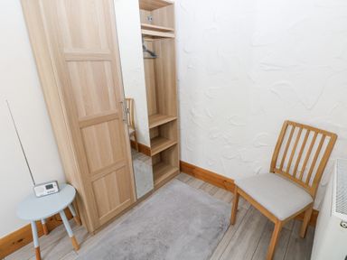 A room corner with a wooden chair a wooden wardrobe a small round table with a radio and a gray rug on a wooden floor at 3 The Barn in Haverfordwest