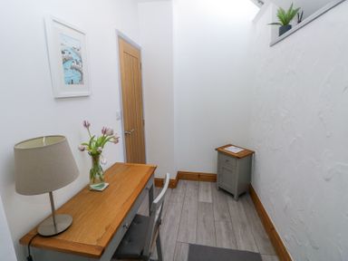 A narrow room with a wooden desk lamp chair small cabinet and framed picture at 3 The Barn in Haverfordwest