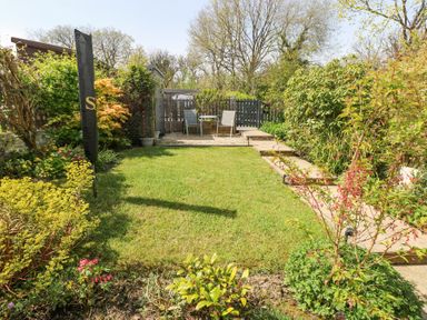A garden with lawn, a seating area with two chairs and a table, plants, and a shed at 3 The Barn in Haverfordwest
