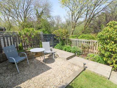 An outdoor seating area with two chairs and a round table on gravel next to a garden path and wooden fence at 3 The Barn in Haverfordwest