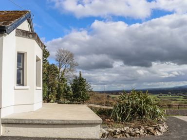 A concrete patio next to a white building with a garden and trees overlooking fields at Heatherbell House Ballyhoura near Buttevant