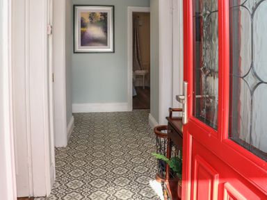An entrance hallway with patterned floor tiles a red door a small wooden table with plants and a framed picture on the wall at Heatherbell House Ballyhoura near Buttevant