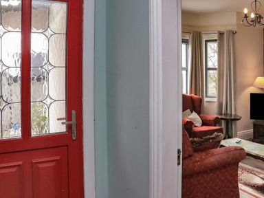 A red front door next to a living room with red armchairs a coffee table and a television at Heatherbell House Ballyhoura near Buttevant