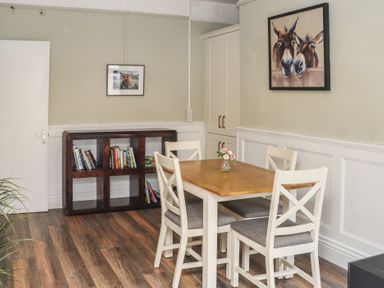A dining room with a wooden table and four chairs a small vase with flowers on the table a dark wooden bookshelf with books two framed animal paintings on the walls at Heatherbell House Ballyhoura near Buttevant