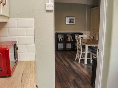 A dining area with a table and four chairs next to a bookshelf and a red microwave on a wooden counter at Heatherbell House in Ballyhoura near Buttevant