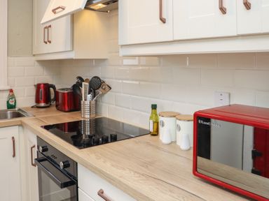 A kitchen countertop with a black stovetop a red microwave oven a bottle of oil two canisters kitchen utensils a red toaster a red electric kettle and a sink at Heatherbell House Ballyhoura near Buttevant
