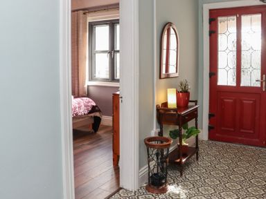 A hallway with a red door a wooden side table with a lamp and plants and a view into a bedroom with a bed and window at Heatherbell House Ballyhoura near Buttevant