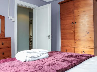 A bedroom with a wooden wardrobe a matching chest of drawers and a bed with a purple cover and folded white towels at Heatherbell House Ballyhoura near Buttevant