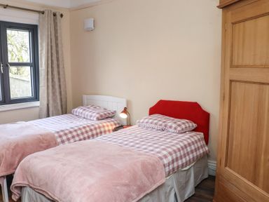 A bedroom with two single beds with checkered bedding and pink blankets a bedside lamp and a wooden wardrobe at Heatherbell House in Ballyhoura near Buttevant