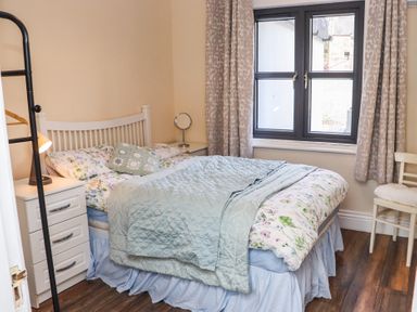 A bedroom with a bed blue bedding floral sheets beside a window with curtains and a chair at Heatherbell House Ballyhoura near Buttevant
