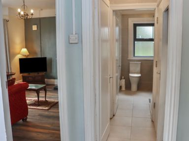 A hallway with doors leading to a bathroom and a living room with a TV and a red sofa at Heatherbell House in Ballyhoura near Buttevant