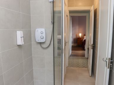 A shower area with wall-mounted soap dispensers and a shower unit looking into a hallway and a bedroom with a bedside lamp at Heatherbell House in Ballyhoura near Buttevant