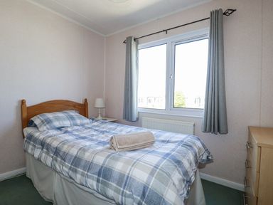 A bedroom with a bed, lamp, and window at Lazy Days in St Merryn