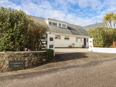 A white house with a grey roof and gravel driveway surrounded by bushes at Coastmans Nest in Mawgan Porth