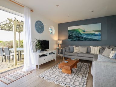 A living room with a wooden coffee table on a patterned rug and a gray sofa at Coastmans Nest in Mawgan Porth