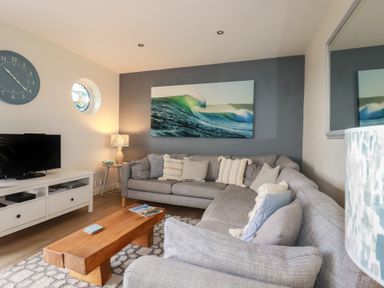A living room with a grey sectional sofa and a wooden coffee table with magazines at Coastman's Nest in Mawgan Porth