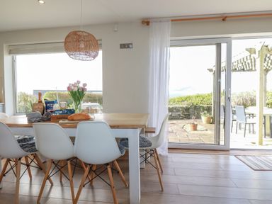 A dining area with white chairs around a wooden table and a glass door leading to an outdoor patio at Coastman's Nest in Mawgan Porth